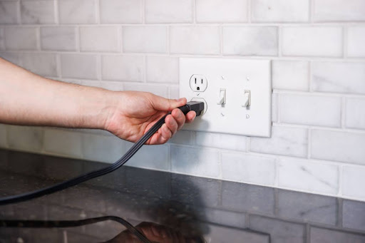 A hand inserting a plug into an electrical outlet.