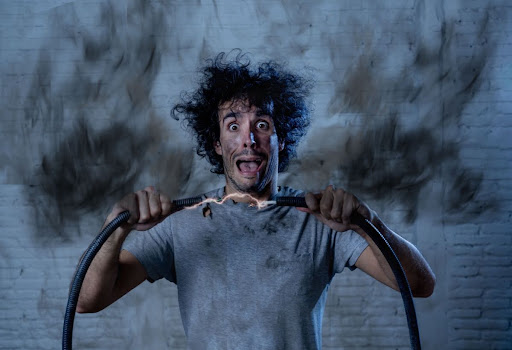 Man holding two smoking wires during an electrical disaster.